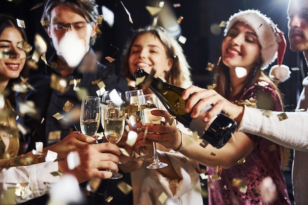 Derramando champanhe. Grupo de amigos alegres comemorando o ano novo dentro de casa com bebidas nas mãos.