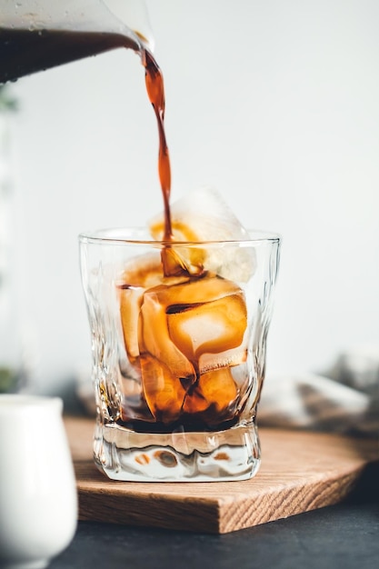 Derramando expresso frio em um copo com cubos de gelo em uma cozinha moderna pela manhã