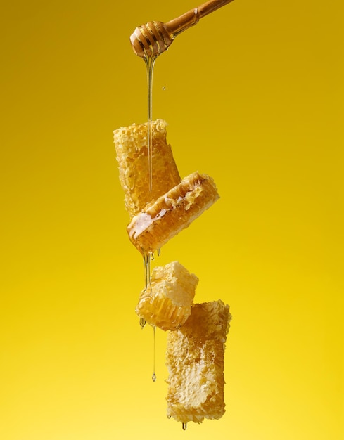 Foto derramando mel doce transparente de um bastão de madeira em um favo de cera de fundo amarelo