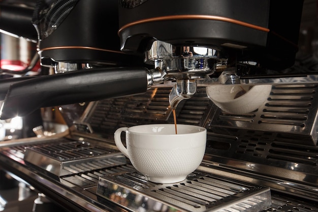 Derramando o fluxo de café da máquina profissional na xícara Barista fazendo café expresso usando o suporte do filtro Café moído fresco fluindo