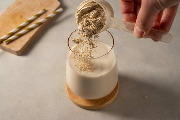 Derramando proteína em pó da colher no copo com milk-shake