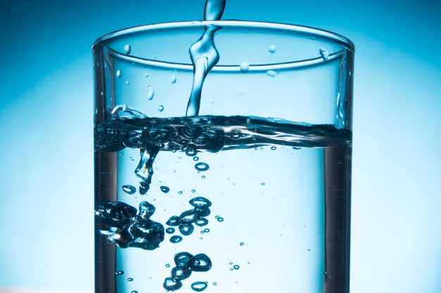 Foto derramar a água no vidro no fundo azul.