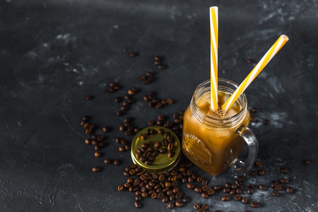 Derramar o leite em um copo de café aromático saboroso frio com gelo no escuro