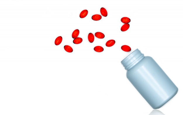 Derrame os comprimidos macios vermelhos da cápsula do gel fora da garrafa da droga isolada. Cápsulas de gelatina macia vermelha vitaminas e suplementos alimentares. Indústria farmacêutica.