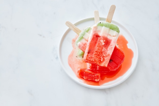 Derretir helado de frutas en un palo con salpicaduras en un plato