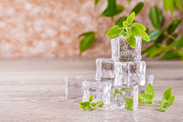 Derritiendo cubitos de hielo y hojas de menta en una mesa de madera