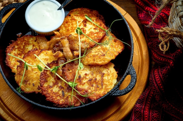 Deruny ucraniano tradicional com creme azedo em uma panela preta Cozinha ucraniana Panqueca de batata Close-up