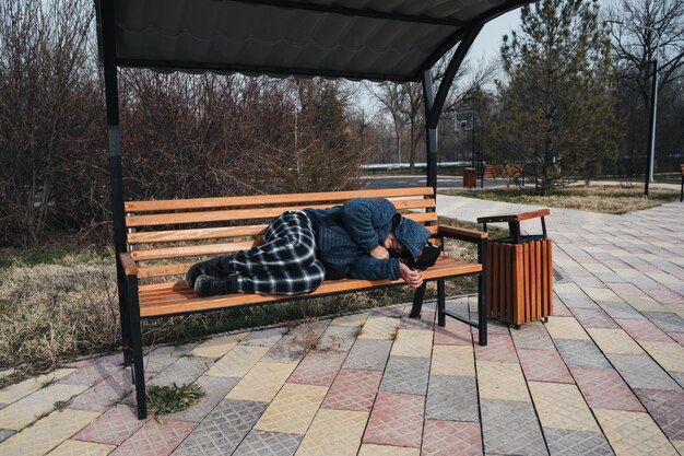 Desabrigado, velho e sujo, homem caucasiano, deitado a dormir num banco do parque no outono.