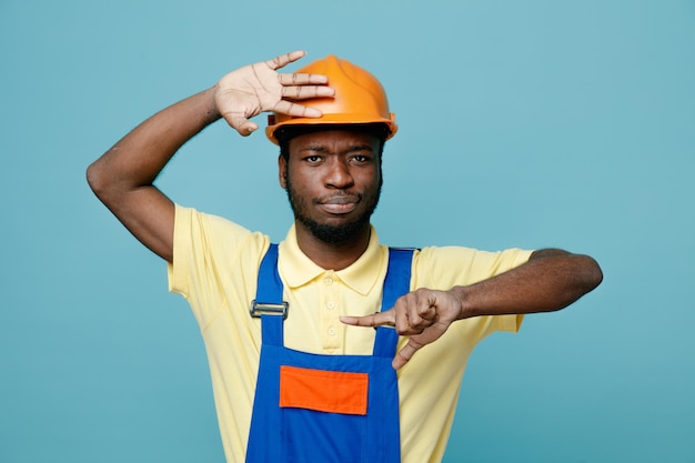 Desagradado mostrando tamanho jovem construtor americano africano de uniforme isolado em fundo azul