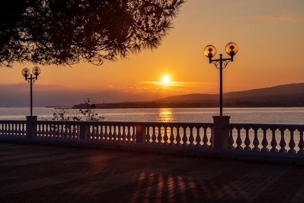 desarmado en el terraplén del resort con balaustrada y linternas. El sol se pone en las montañas y se refleja en el mar. Rama de pino en primer plano.El Resort Of Gelendzhik.