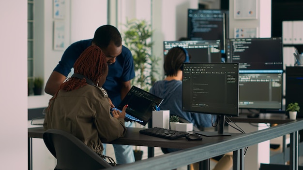 Desarrollador de bases de datos explicando el algoritmo a un colega codificador que señala el código en ejecución en una computadora portátil. Ingenieros de sistemas que colaboran en el proyecto del grupo de desarrollo, utilizando la ventana de terminal.