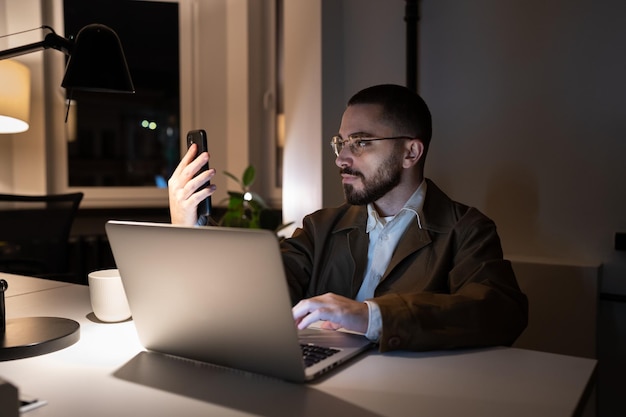 El desarrollador de front-end ocupado o la aplicación de prueba del ingeniero de qa en el teléfono inteligente trabajan horas extras en el espacio de coworking