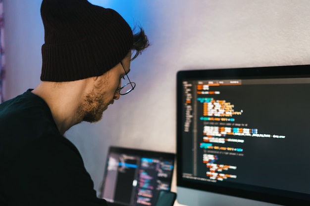 El desarrollador móvil joven escribe el código del programa en una computadora, el programador trabaja en la oficina en casa.