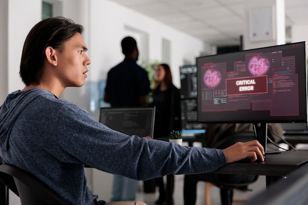 Desarrollador de software preocupado por haber pirateado el servidor web, mirando un error crítico en la pantalla de la computadora en la oficina de programación. Desarrollador web asiático tratando de resolver problemas de piratería, seguridad de cortafuegos.