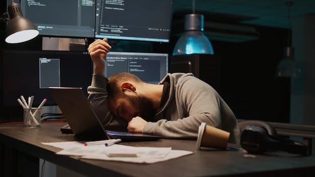 Desarrollador de TI bostezando y quedándose dormido en el escritorio, exhausto e intentando trabajar en una nueva programación de interfaz. El hombre se siente somnoliento y cansado a altas horas de la noche, usando el código del servidor. Disparo de mano.