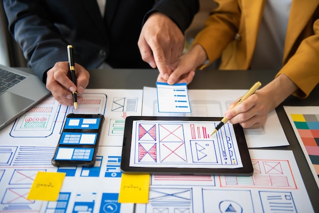 El desarrollador de UX y el diseñador de UI hacen una lluvia de ideas sobre el diseño de estructura alámbrica de la interfaz de la aplicación móvil con el resumen del cliente y el código de color en officexA
