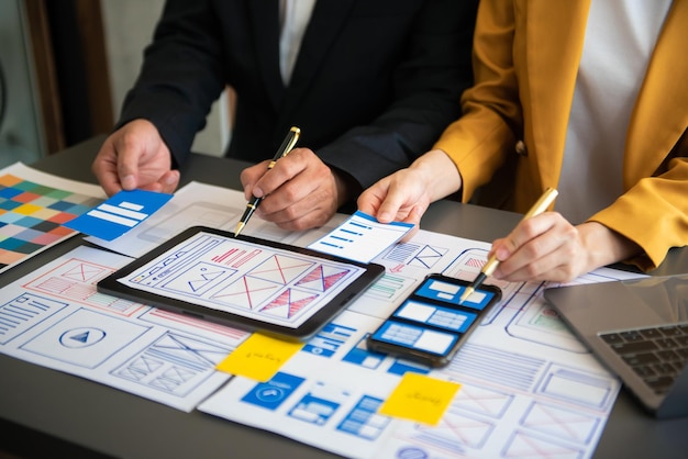 El desarrollador de UX y el diseñador de UI hacen una lluvia de ideas sobre el diseño de estructura alámbrica de la interfaz de la aplicación móvil con el resumen del cliente y el código de color en officexA