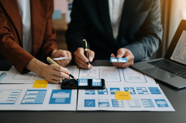 El desarrollador de UX y el diseñador de UI hacen una lluvia de ideas sobre el diseño de estructura alámbrica de la interfaz de la aplicación móvil con el resumen del cliente y el código de color en officexA