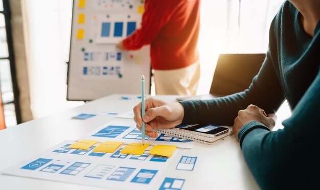 Desarrollador de UX y diseñador de UI haciendo una lluvia de ideas sobre el diseño de wireframe de la interfaz de la aplicación móvil con el breif del cliente y el código de color en la oficina moderna