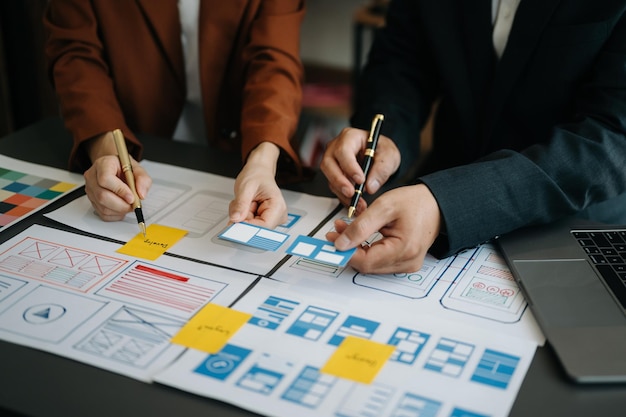 Desarrollador de UX y diseñador de UI haciendo una lluvia de ideas sobre el diseño de wireframe de la interfaz de la aplicación móvil con el breif del cliente y el código de color en la oficina moderna