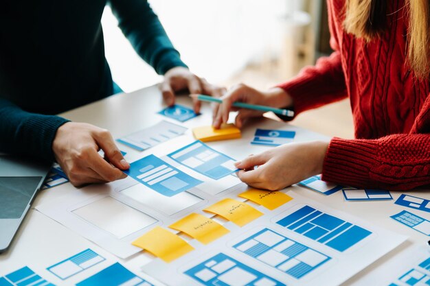 Desarrollador de UX y diseñador de UI haciendo una lluvia de ideas sobre el diseño de wireframe de la interfaz de la aplicación móvil con el breif del cliente y el código de color en la oficina