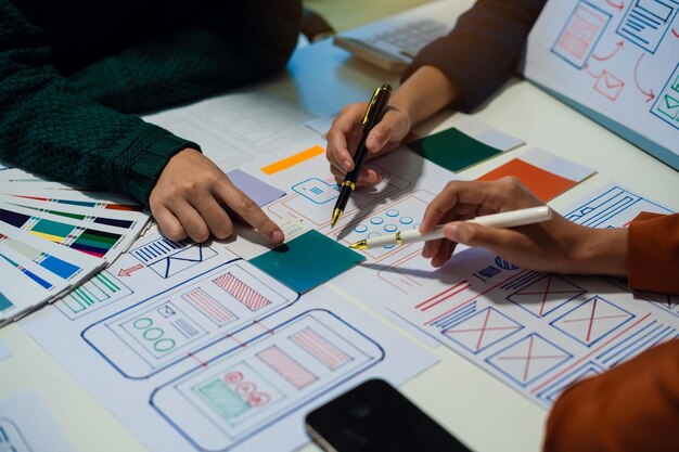 Desarrollador de UX y diseñador de UI haciendo una lluvia de ideas sobre el diseño de wireframe de la interfaz de la aplicación móvil con el breif del cliente y el código de color en la oficina