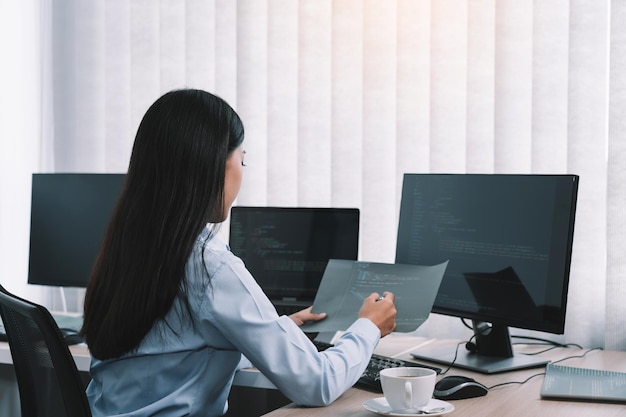 Desarrolladoras de software asiáticas sentadas frente a las computadoras mirando los códigos de la computadora en la pantalla