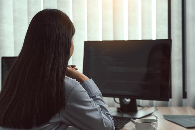 Desarrolladoras de software asiáticas sentadas frente a las computadoras mirando los códigos de la computadora en la pantalla