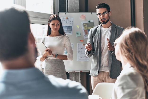 Desarrollando nueva estrategia. Dos jóvenes colegas que realizan presentaciones mientras trabajan con su equipo de negocios en la oficina.