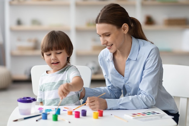 Desarrollo del arte en casa niño feliz pintando con una madre joven y hermosa y riendo disfrutando