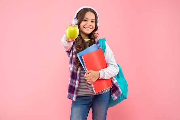 Desarrollo infantil. el niño en los auriculares sostiene el libro de trabajo y la mochila. educación en línea. De vuelta a la escuela. chica adolescente positiva en auriculares con manzana. escuchar música. nueva tecnología.