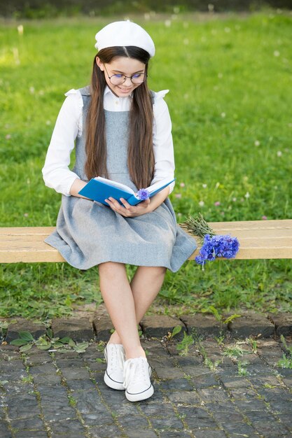 Desarrollo de la lectura. Un niño pequeño lee un libro en un banco del parque. Desarrollo infantil. Habilidades de aprendizaje y dominio. Escuela y educación. Crecimiento y desarrollo. Desarrollo personal.