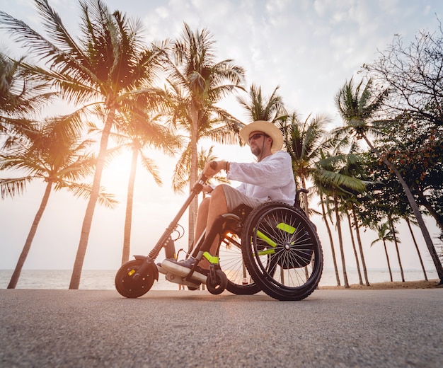 Desativado o homem em uma cadeira de rodas com scooter elétrico na praia