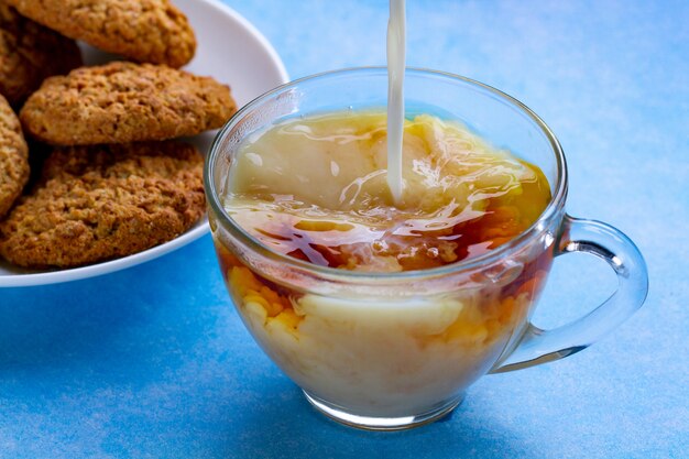 Desayune con galletas de avena y vierta leche en una taza de té negro. Harina, postre de cereales y bebida caliente.