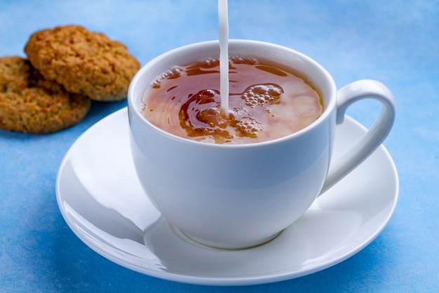 Desayune con galletas de avena y vierta leche en una taza de té negro. Harina, postre de cereales y bebida caliente.