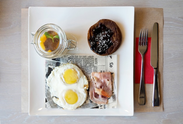 Desayune con los huevos fritos, el tocino, la crepe y el yogur en la placa blanca.