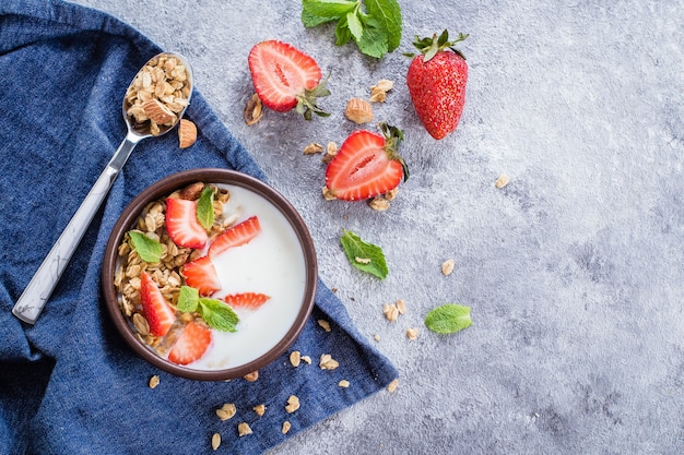 Desayune con el yogur, el granola del muesli y las fresas en fondo concreto gris de la tabla.