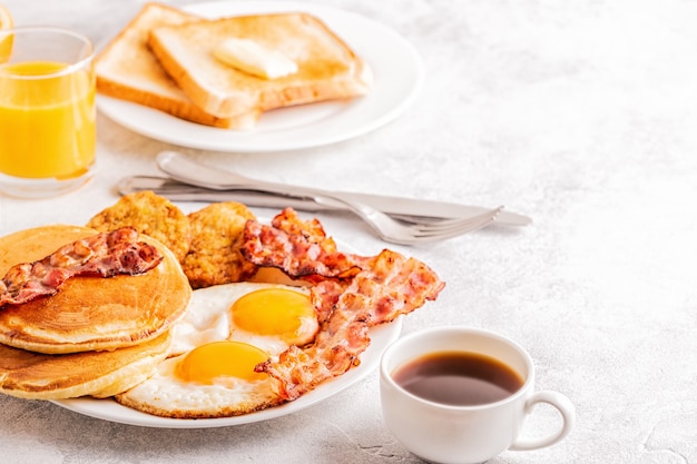 Desayuno americano completo saludable con huevos, tocino, panqueques y latkes, enfoque selectivo.