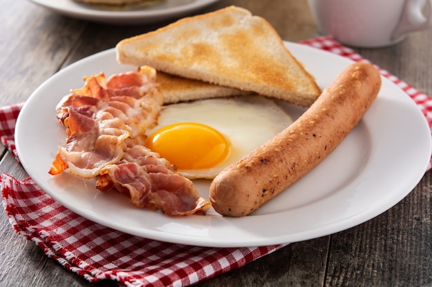 Desayuno americano tradicional con huevo frito, tostadas, tocino y salchichas en mesa de madera