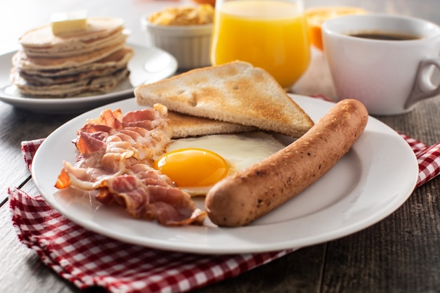 Desayuno americano tradicional con huevo frito, tostadas, tocino y salchichas en mesa de madera