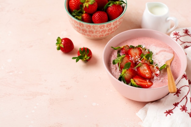 Desayuno con batido de granola, coco y fresa en un bol sobre un fondo rosa claro. Menú de dieta de primavera Vista superior.