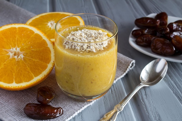 Desayuno con batido de naranja, dátiles y copos de avena sobre el fondo de madera gris