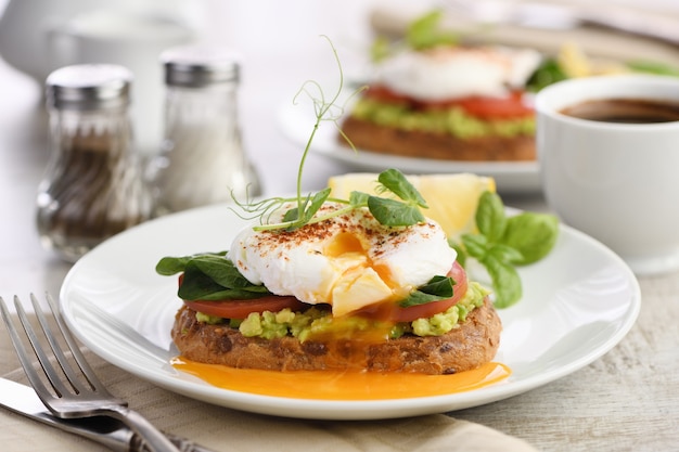 Desayuno. Best Eggs Benedict sobre una rebanada de pan de cereal tostado con guacamole y espinacas