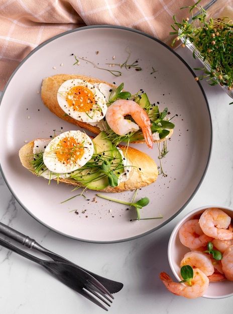 Desayuno con bruschetta con camarones, huevos y microgreens en un plato, cerrar