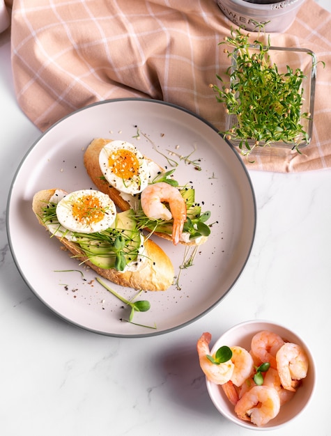 Desayuno con bruschetta con camarones, huevos y microgreens en un plato, cerrar