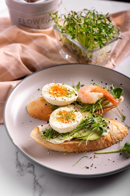 Desayuno con bruschetta con camarones, huevos y microgreens en un plato, cerrar