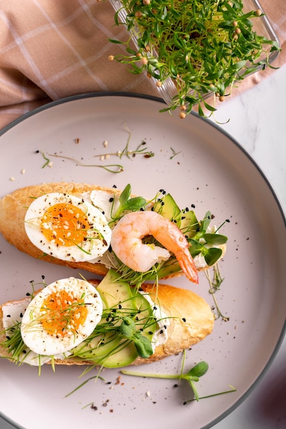 Desayuno con bruschetta con camarones, huevos y microgreens en un plato, cerrar