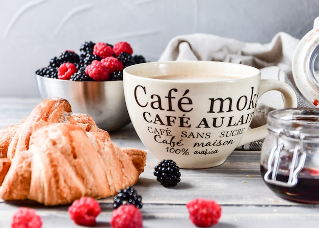 Desayuno café con leche y cruasanes, mermelada y frambuesas frescas y moras