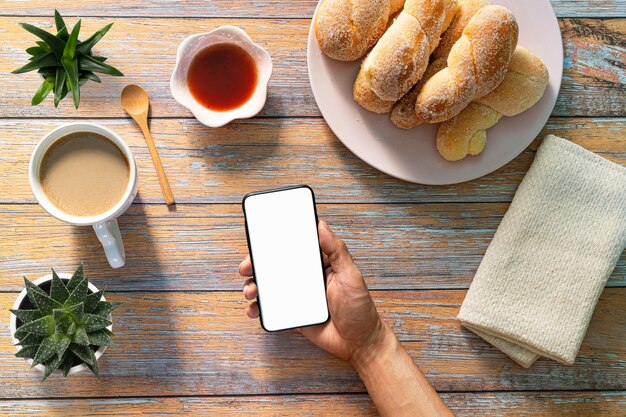 Desayuno con café y pan en la mesa con el teléfono Tomando foto de recién horneado