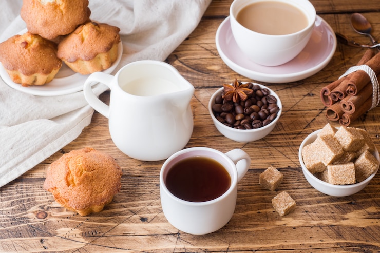 Desayuno y café, pasteles, azúcar moreno y canela con anís sobre madera.